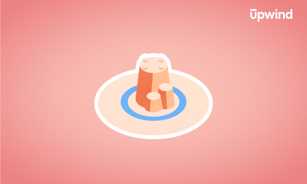 An illustration of a smiling sandcastle with two small towers on a circular sandy area, set against a pink background. The word Upwind appears in the top right corner.